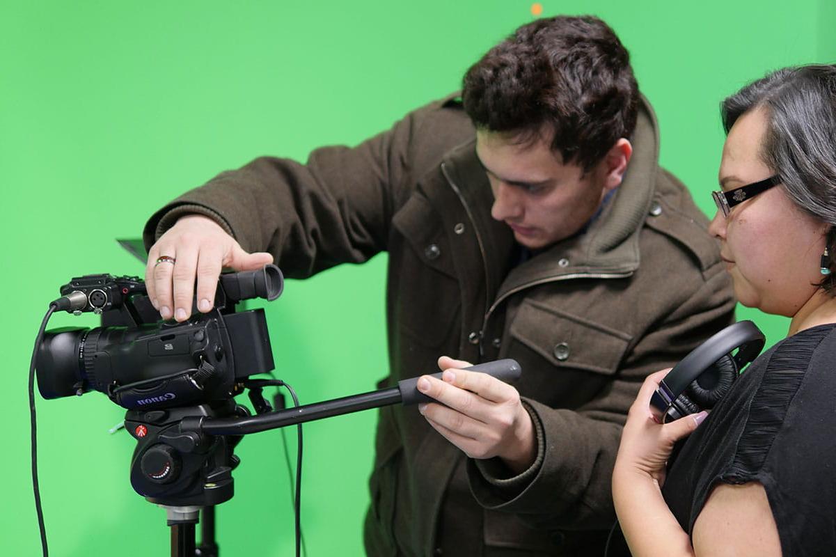 Two individuals work with a camera in front of a green screen